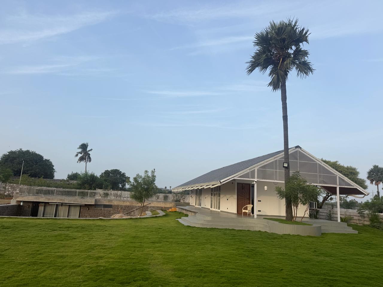 Ikshvaku Vanam farmhouse and palm tree, with the stone level below, across the lawn